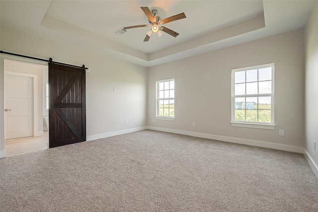 spare room featuring a tray ceiling, a barn door, and light carpet