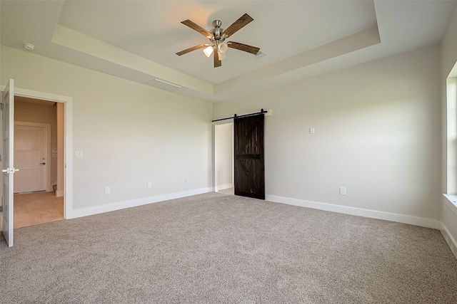 unfurnished bedroom featuring light carpet, a barn door, a raised ceiling, and ceiling fan