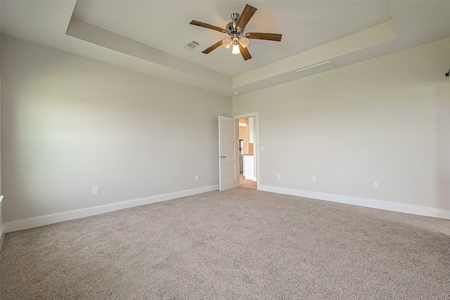 carpeted spare room with ceiling fan and a raised ceiling