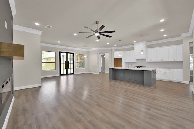 kitchen with a large island with sink, white cabinetry, light hardwood / wood-style floors, decorative light fixtures, and ornamental molding