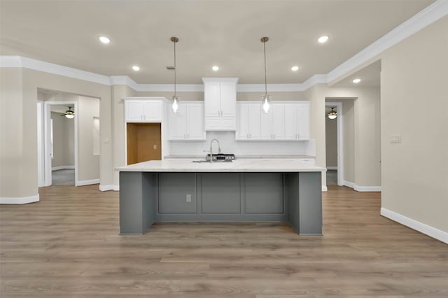 kitchen featuring ornamental molding, white cabinetry, sink, and a large island with sink