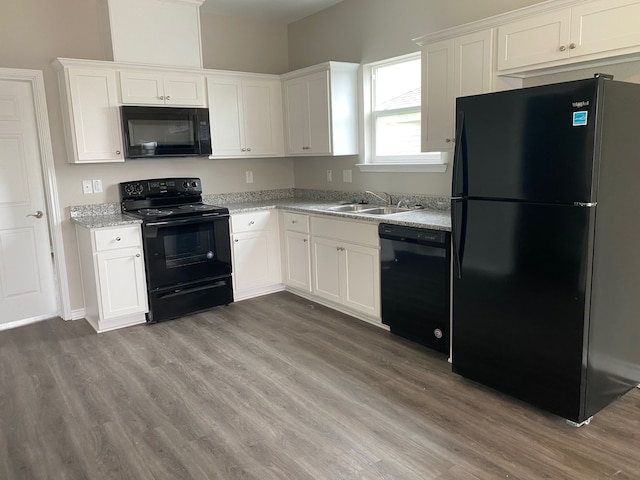 kitchen with light stone countertops, black appliances, white cabinetry, and hardwood / wood-style flooring