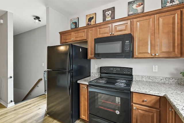 kitchen featuring light stone counters, light wood-type flooring, and black appliances