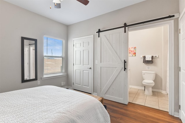 bedroom featuring dark hardwood / wood-style floors, a barn door, ensuite bathroom, and ceiling fan