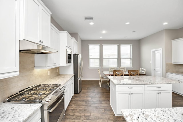 kitchen with stainless steel appliances, a kitchen island, light stone counters, dark hardwood / wood-style floors, and white cabinets