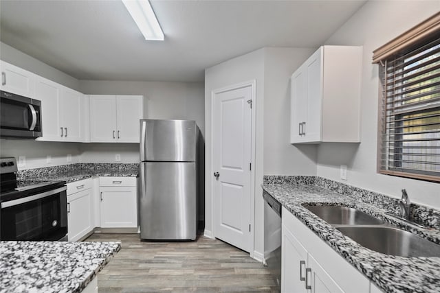 kitchen featuring stone counters, appliances with stainless steel finishes, sink, white cabinets, and light hardwood / wood-style flooring