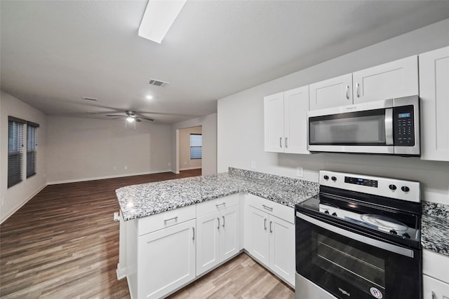 kitchen with appliances with stainless steel finishes, kitchen peninsula, white cabinets, and light hardwood / wood-style floors