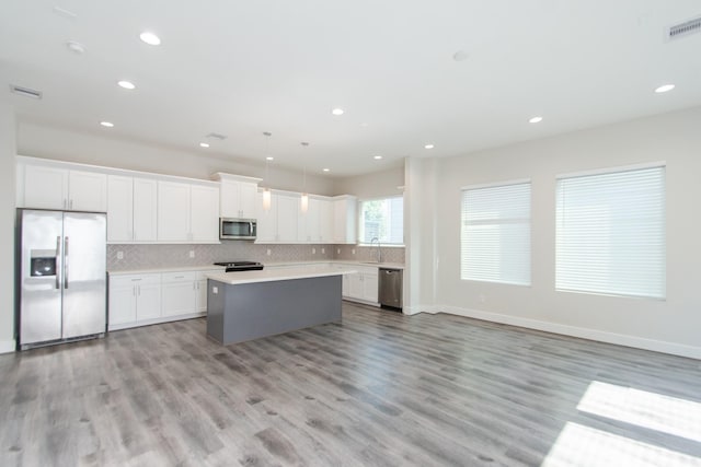 kitchen with appliances with stainless steel finishes, decorative light fixtures, a kitchen island, and white cabinets