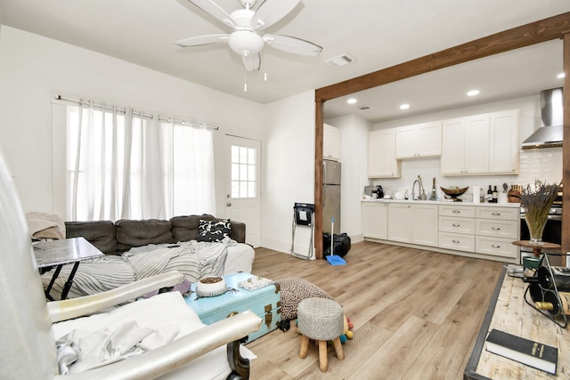 living room featuring light hardwood / wood-style floors, beamed ceiling, sink, and ceiling fan