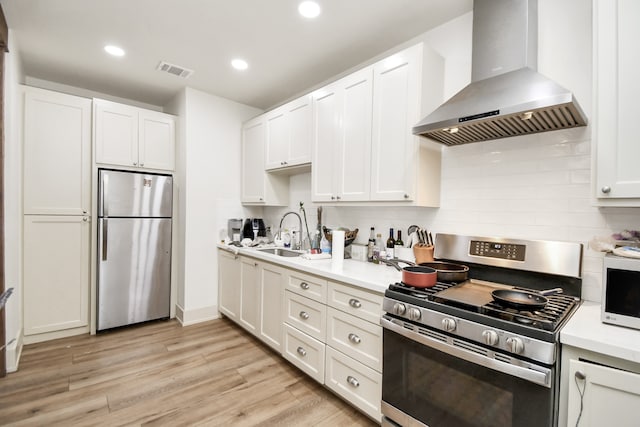 kitchen featuring wall chimney range hood, light hardwood / wood-style flooring, stainless steel appliances, and sink