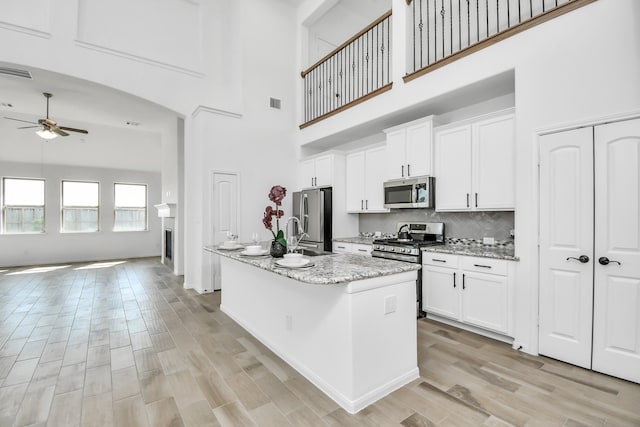 kitchen featuring light stone counters, stainless steel appliances, a high ceiling, and a kitchen island with sink