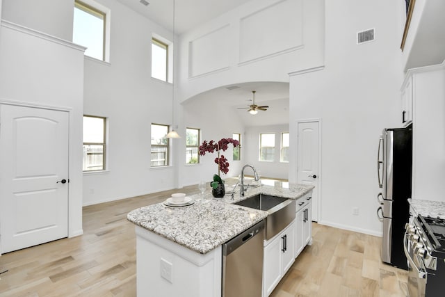 kitchen featuring a towering ceiling, appliances with stainless steel finishes, sink, an island with sink, and white cabinetry