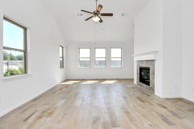 unfurnished living room featuring a high ceiling, a tile fireplace, light wood-type flooring, and ceiling fan