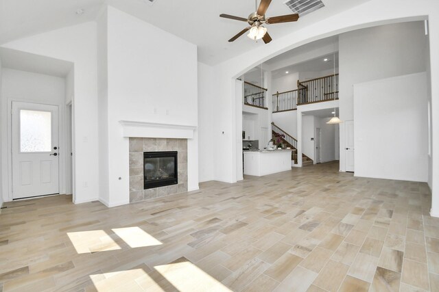 unfurnished living room with light hardwood / wood-style flooring, a tiled fireplace, high vaulted ceiling, and ceiling fan