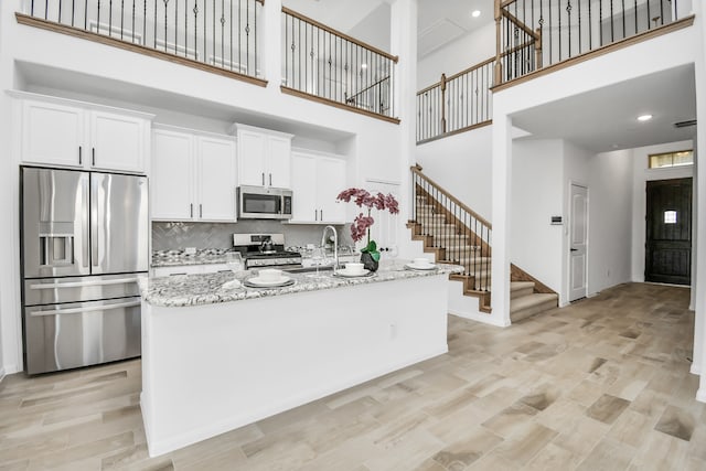 kitchen featuring a center island with sink, a high ceiling, white cabinets, and stainless steel appliances