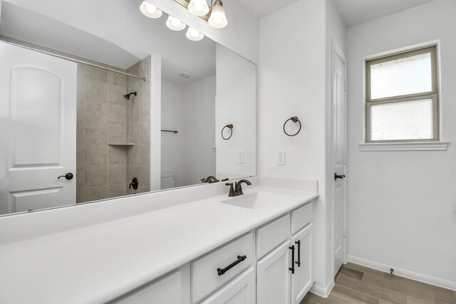 bathroom featuring vanity, hardwood / wood-style floors, a tile shower, and toilet