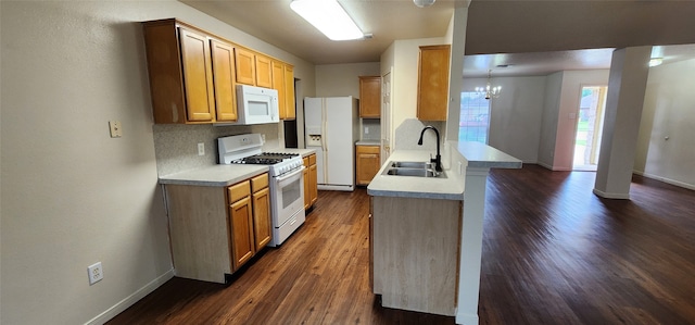 kitchen with white appliances, sink, hanging light fixtures, dark wood-type flooring, and an inviting chandelier