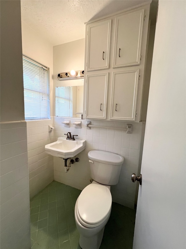 bathroom with toilet, a textured ceiling, sink, and tile walls