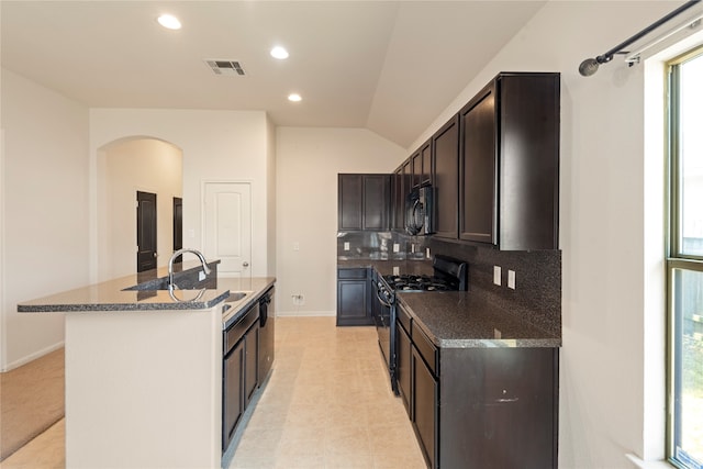 kitchen featuring lofted ceiling, decorative backsplash, a kitchen island with sink, sink, and black appliances