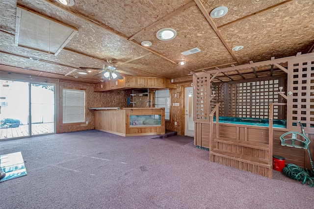 unfurnished living room featuring ceiling fan, wooden walls, and carpet floors