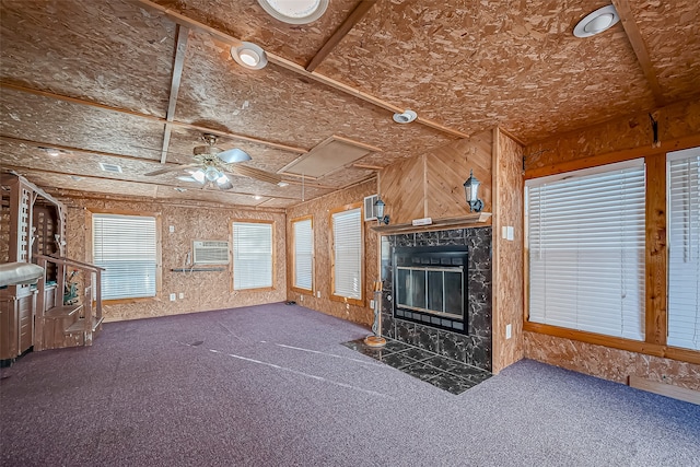 unfurnished living room with ceiling fan, a fireplace, and dark colored carpet