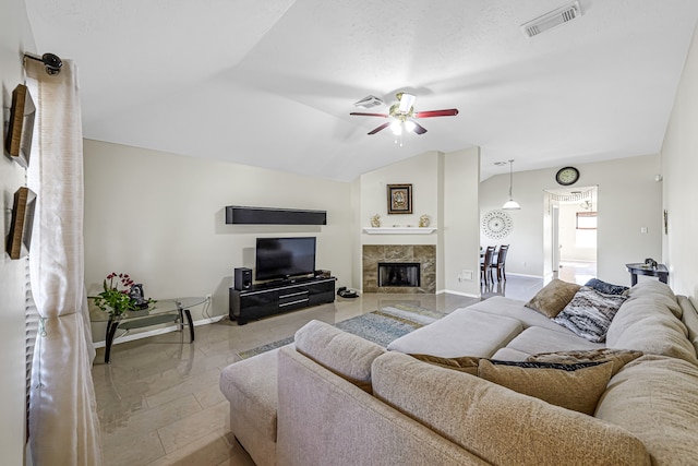 living room featuring ceiling fan, a tiled fireplace, and vaulted ceiling