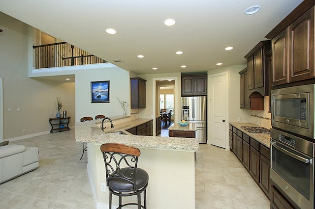 27827 Ramble Rock Ct, Katy, TX 77494 - kitchen featuring appliances with stainless steel finishes, a breakfast bar, a sink, recessed lighting, and dark brown cabinetry