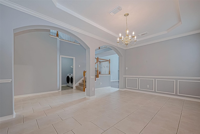 tiled empty room with a tray ceiling, ornamental molding, washer and dryer, and a notable chandelier