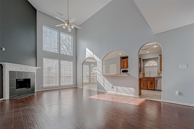 unfurnished living room with a tile fireplace, ceiling fan, sink, and high vaulted ceiling