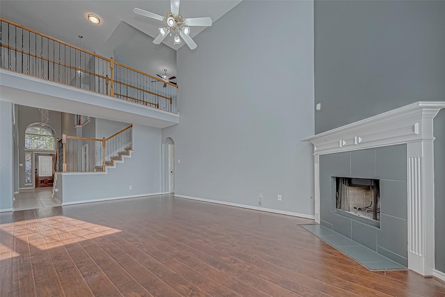 unfurnished living room with ceiling fan, wood-type flooring, a towering ceiling, and a tile fireplace