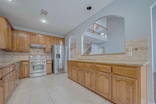 kitchen with sink, light stone counters, decorative backsplash, light tile patterned floors, and appliances with stainless steel finishes