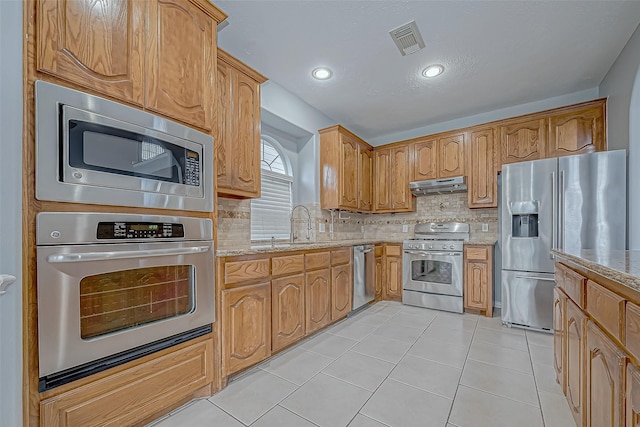 kitchen featuring light stone countertops, sink, stainless steel appliances, decorative backsplash, and light tile patterned floors