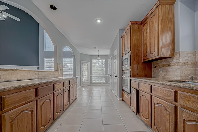 kitchen with backsplash, ceiling fan, appliances with stainless steel finishes, light tile patterned flooring, and light stone counters