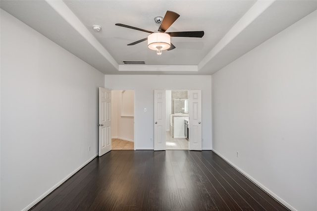 unfurnished bedroom with ceiling fan, a tray ceiling, and dark hardwood / wood-style floors