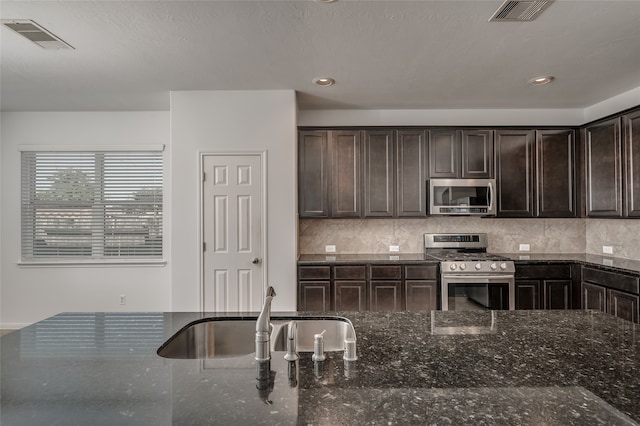 kitchen with backsplash, dark stone countertops, sink, dark brown cabinetry, and appliances with stainless steel finishes