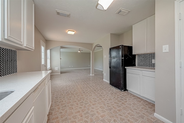 kitchen with white dishwasher, white cabinetry, black refrigerator, and backsplash