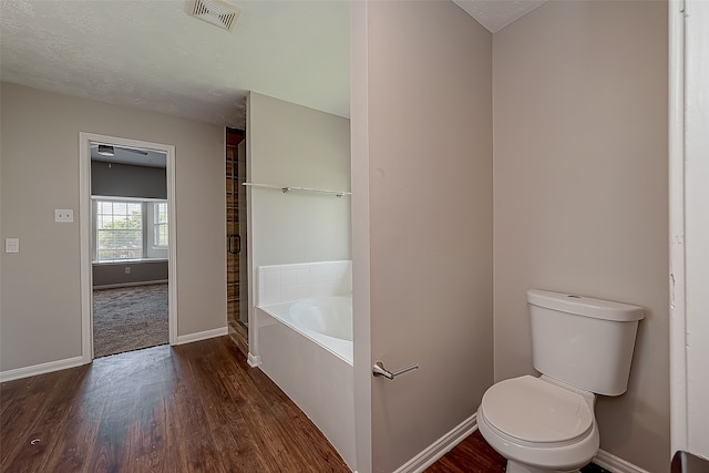 bathroom with wood-type flooring, a textured ceiling, toilet, and a tub