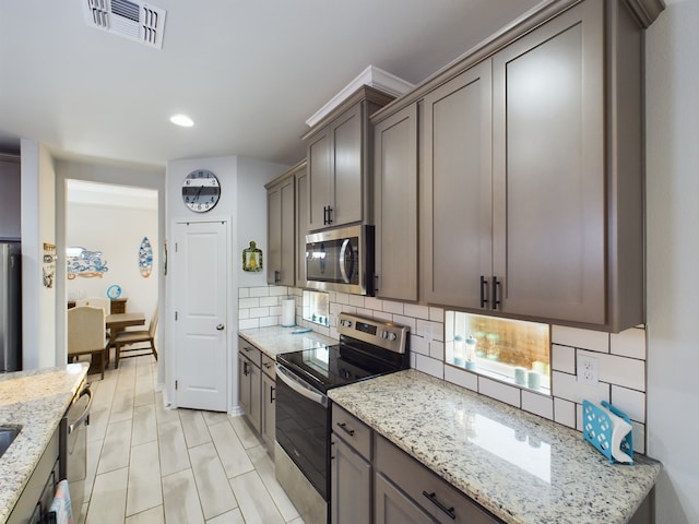 kitchen with light stone countertops, appliances with stainless steel finishes, and backsplash