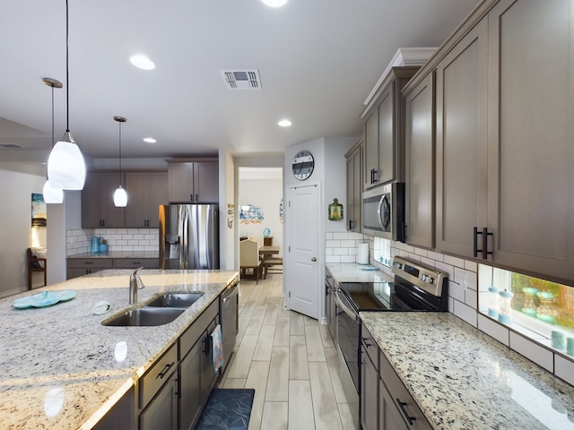 kitchen with light stone counters, stainless steel appliances, tasteful backsplash, sink, and decorative light fixtures