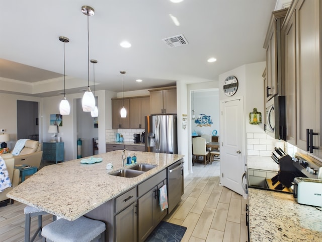 kitchen with appliances with stainless steel finishes, decorative backsplash, sink, and a kitchen island with sink