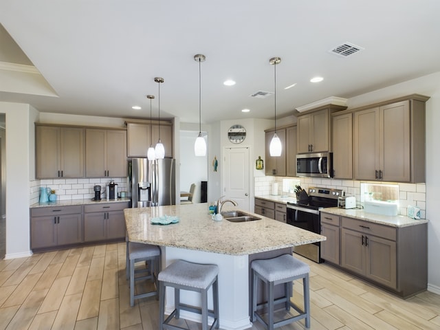 kitchen with a kitchen island with sink, decorative light fixtures, stainless steel appliances, and tasteful backsplash