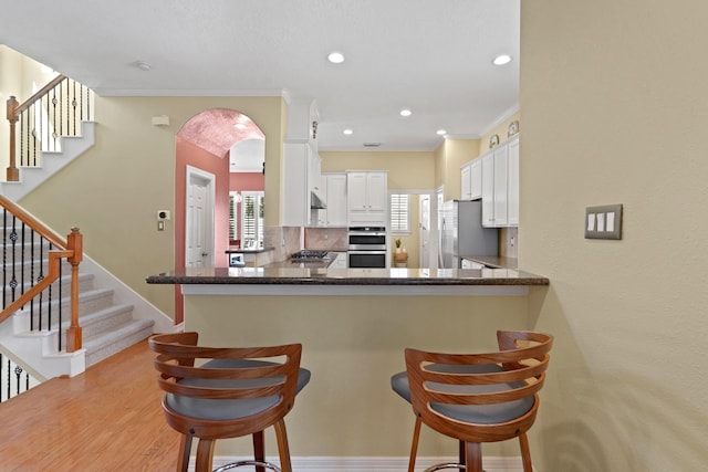 kitchen featuring kitchen peninsula, a kitchen breakfast bar, tasteful backsplash, stainless steel appliances, and white cabinets