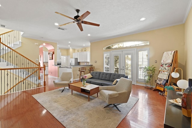 living room featuring french doors, crown molding, ceiling fan, a textured ceiling, and light hardwood / wood-style floors