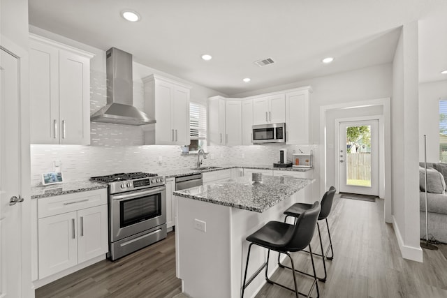 kitchen featuring wall chimney exhaust hood, a kitchen island, appliances with stainless steel finishes, and white cabinets