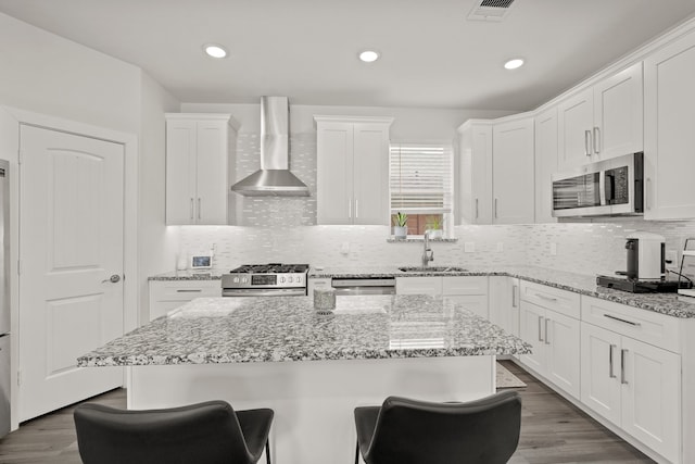 kitchen with sink, a center island, stainless steel appliances, wall chimney exhaust hood, and dark wood-type flooring