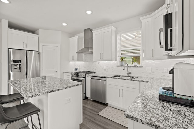 kitchen featuring wall chimney range hood, sink, appliances with stainless steel finishes, a center island, and white cabinetry