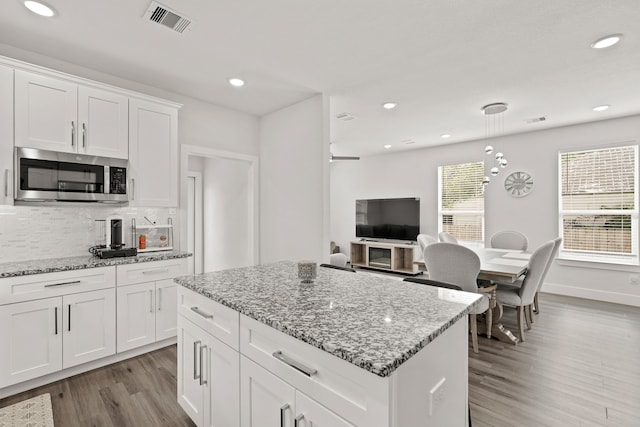 kitchen featuring white cabinetry, light stone counters, decorative backsplash, and light wood-type flooring