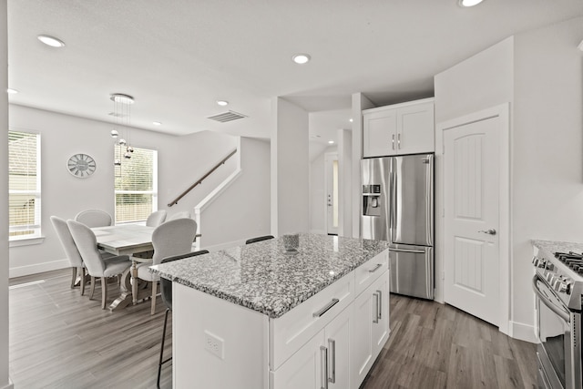 kitchen featuring appliances with stainless steel finishes, light wood-type flooring, a kitchen island, white cabinets, and light stone counters