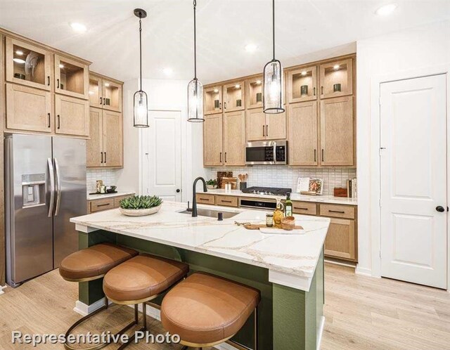 kitchen with light wood-type flooring, sink, decorative backsplash, an island with sink, and appliances with stainless steel finishes