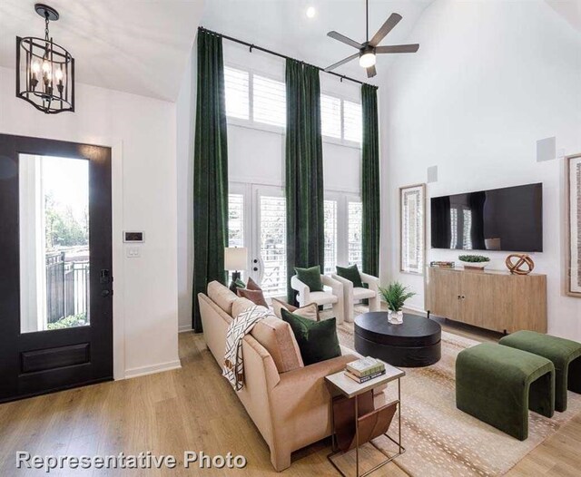 living room with ceiling fan with notable chandelier, light wood-type flooring, and a high ceiling